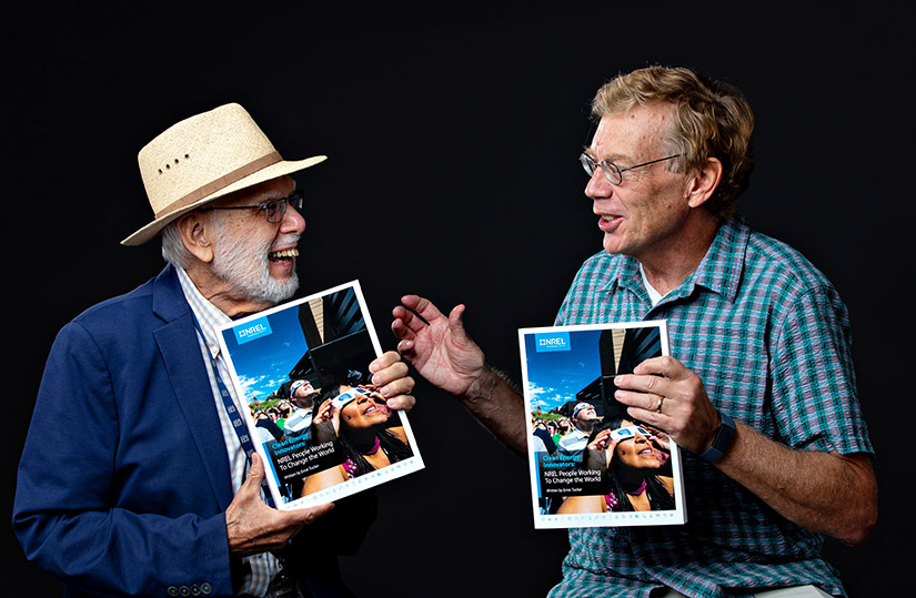 Two people laughing while facing each other and holding up a book.
