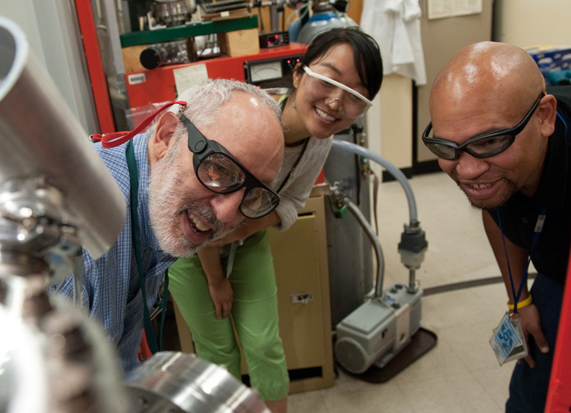 Three researchers look at a piece of scientific equipment in a lab.