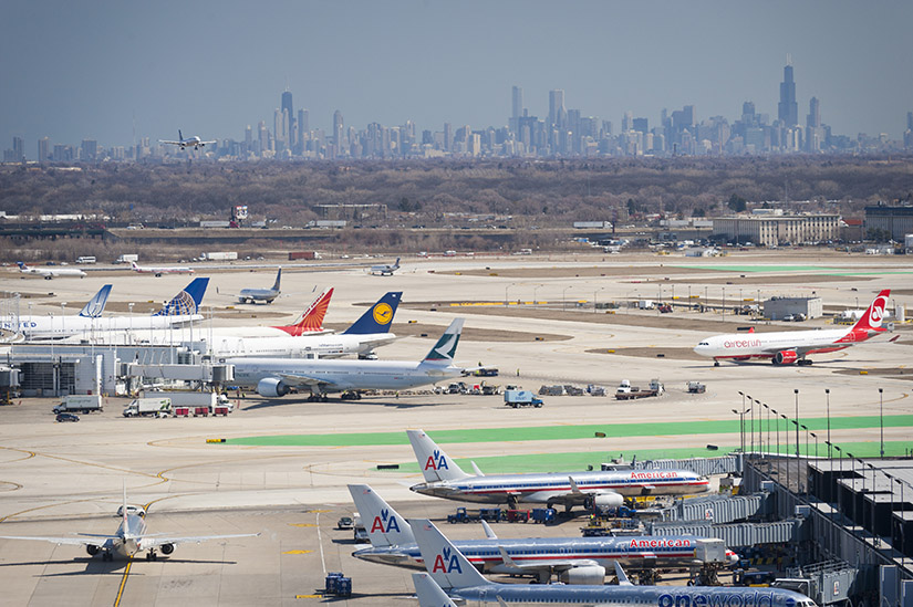 Planes lined up at an airport with Chicago skyline in background.