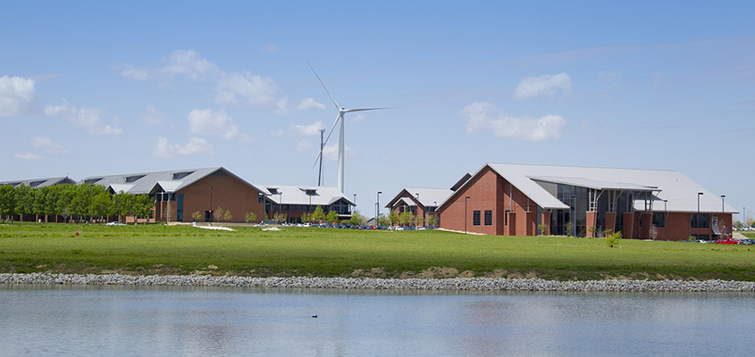 A wind turbine next to a school viewed from across a lake.