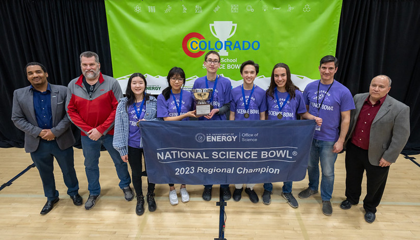 A group stands with the Science Bowl trophy and banner.