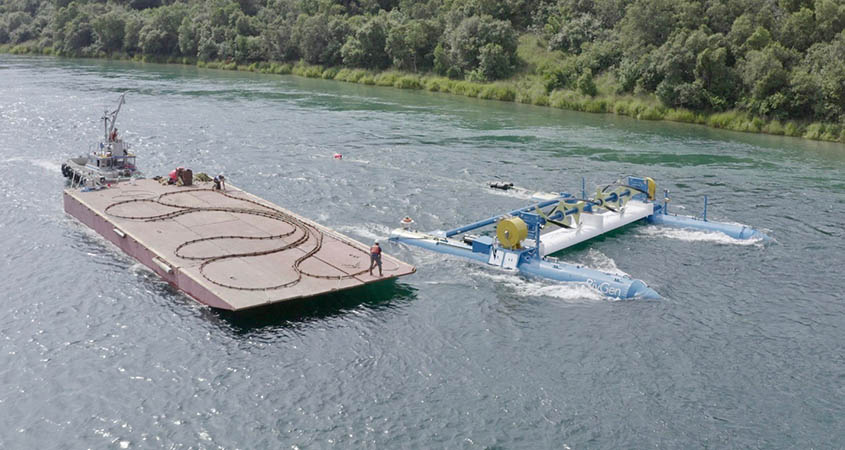 An aerial view of a river with a barge next to a river current device.