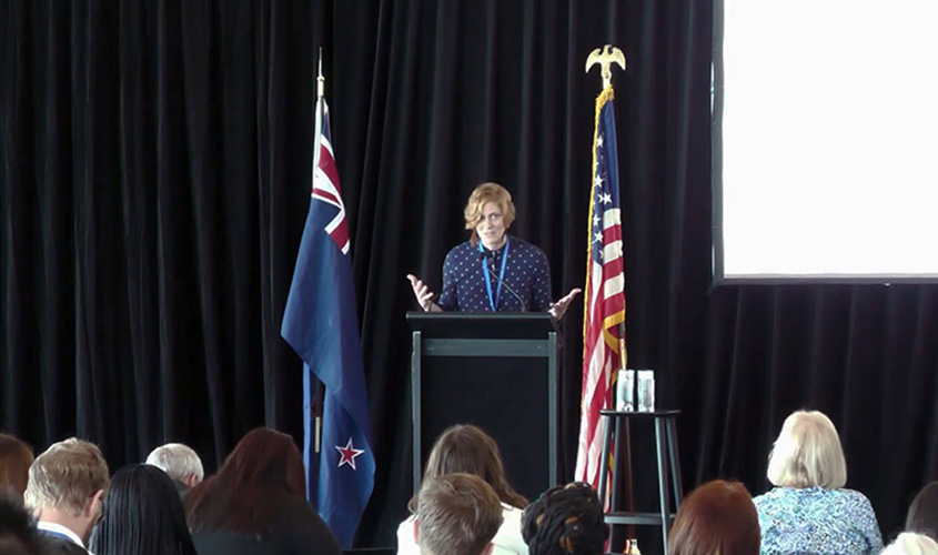 Tessa Greco standing behind a podium on stage with an audience looking on.