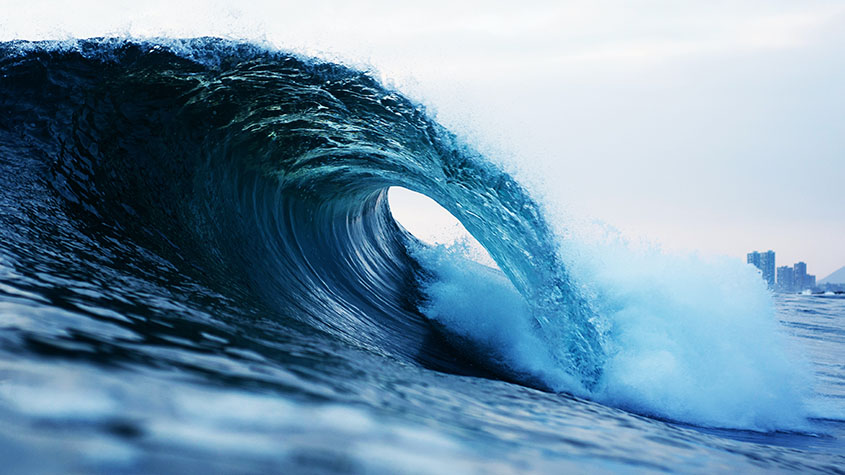 A barrel wave crashes in front of a city skyline.