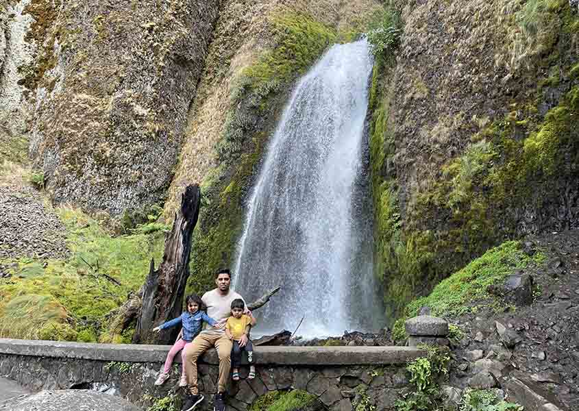 Danish Saleem and two children sitting on a rock wall in front of a waterfall