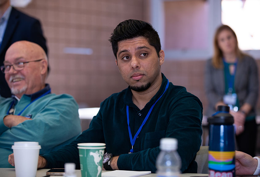 Danish Saleem wearing a name tag and sitting at a table with other researchers.