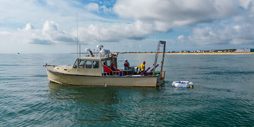 A boat with two crew members reeling in a device shaped like a life saver.