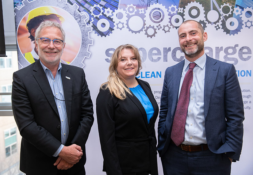 Three people in business clothes in front of the American-Made backdrop.  