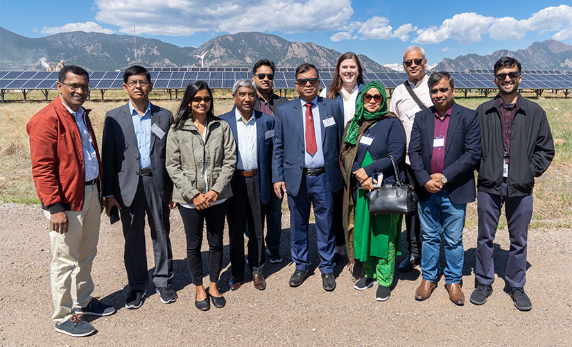 The group of nine smiles for a photo in front of a solar array with the Flatirons rock formations in the background.