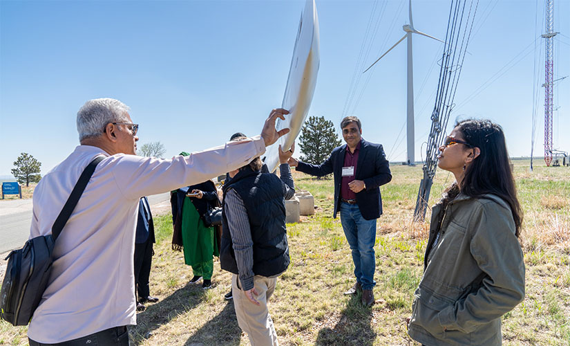 A group views a turbine blade in the grass. A man touches the edge of the blade.