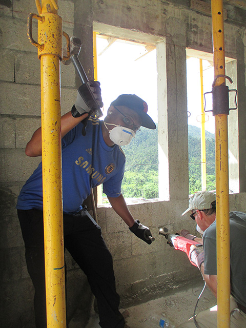 A person standing inside a building looks at the camera and swings a hammer.