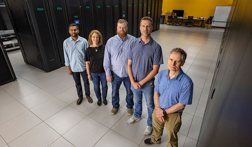 A group of five people pose for a photo in a computer lab.