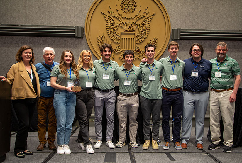 A group of students  standing in front of the U.S. seal in matching shirts and name tags. 