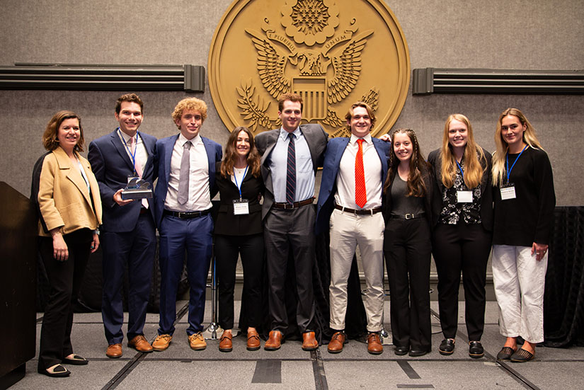 A group of students standing in front of the U.S. seal in business attire. 