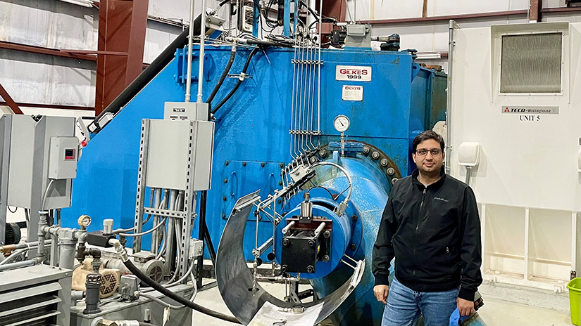 Mayank Panwar standing in front of a large mechanical device in a warehouse