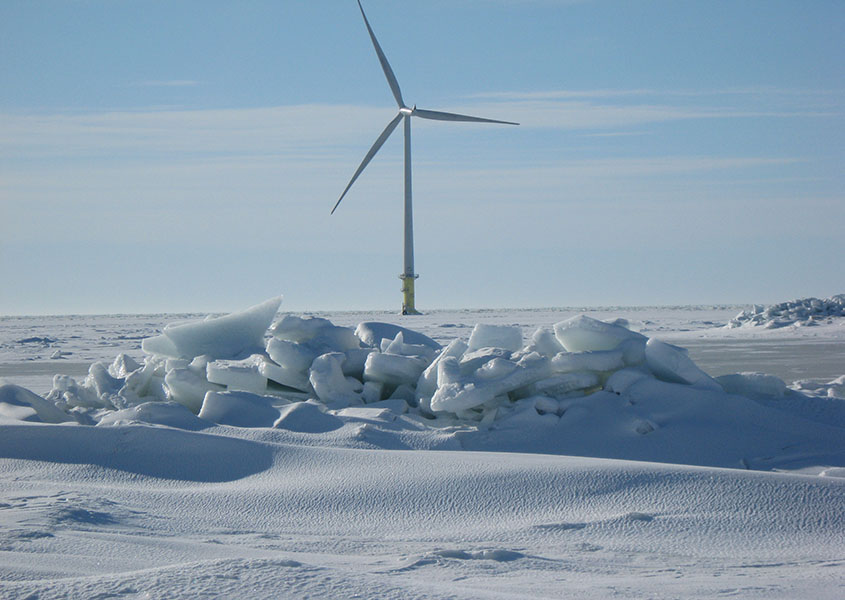 A wind turbine on a frozen body of water with chunks of ice in the foreground.