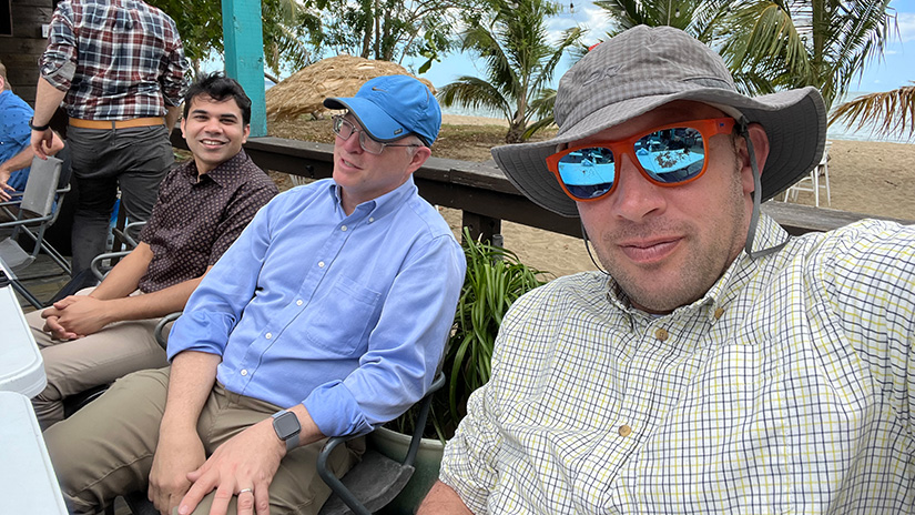 Three people sitting outside in front of a beach.