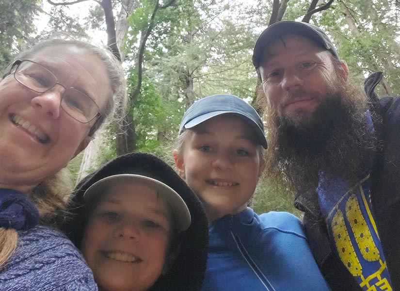 A selfie of Sam, her husband, and her two children in the woods.