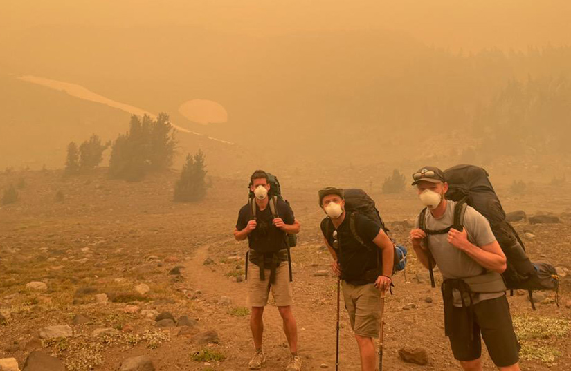 Three people with hiking gear stand on a smoky hillside.