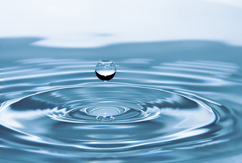 Closeup of a drop of water above a rippled water surface.