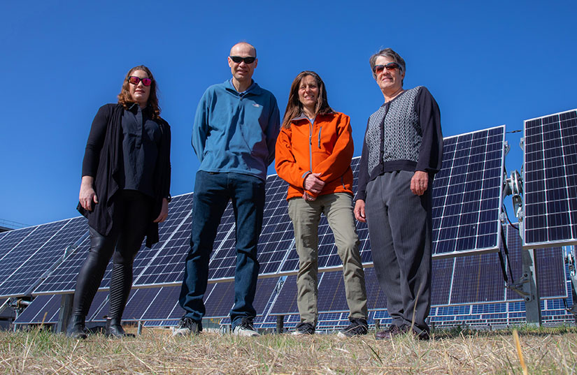 Three women and a man stand in front of a PV array.