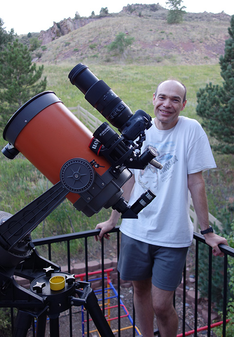 A man stands next to a telescope outdoors.