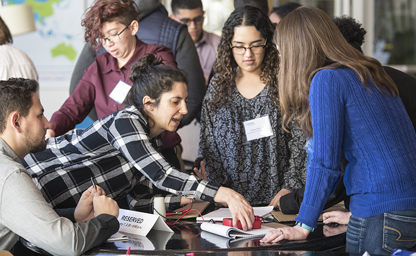  A woman helps a group of young men and women build a mechanical device.