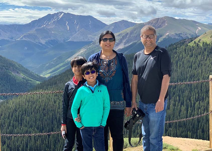 Abhishek standing with his wife and twin boys in front of a valley with pine-tree-covered mountains