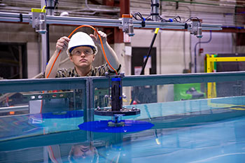 A man holding a wire attached to a small marine energy device floating in a large tank of water