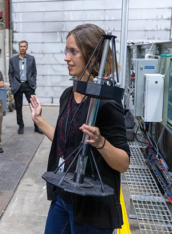 A woman holding a small marine energy device while standing in front of a tank of water