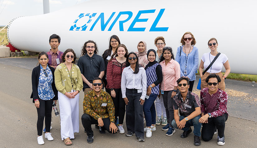 A group of people stands in front of a large NREL logo.