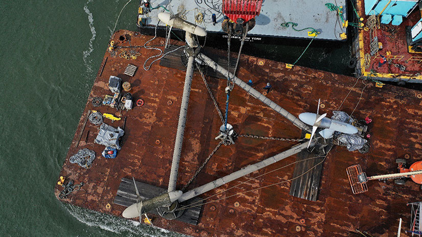 A rusty barge with a triangular frame with three tidal turbines on each point