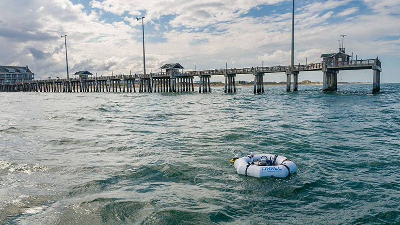 A white raft floats in the ocean with a pier in the background