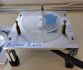 A raised square metal plate with three bolts forming a triangle, within which is a round glass plate.NREL researchers are using Seedling funding to perform benchtop testing of triboelectric nanogenerators, or TENGS, for use in large-scale wave energy converters. Pictured is the team’s rotary TENG prototype on a custom test rig that was built to characterize the power production of a single-layer rotary TENG. Photo by Calum Kenny, NREL