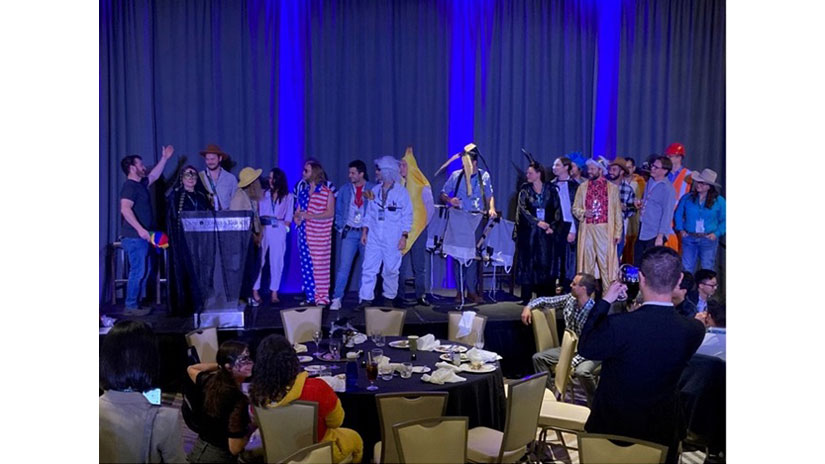 Conference attendees in costumes stand on a stage