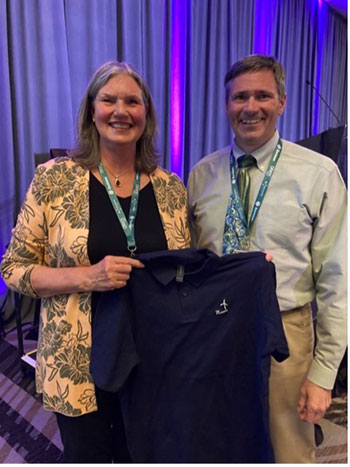 Sue Hock holds up a polo shirt that reads “?-oneer.” Tom Acker stands next to her.