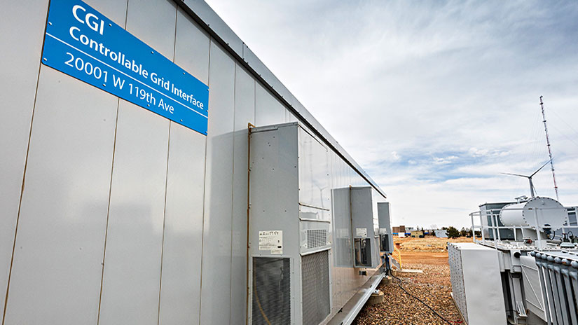 A small building with machinery and a wind turbine in the background