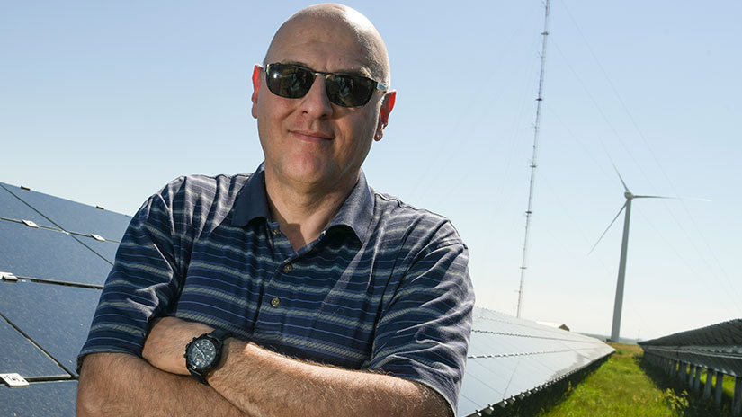 Vahan Gevorgian in sunglasses standing in front of solar photovoltaic panels and a wind turbine