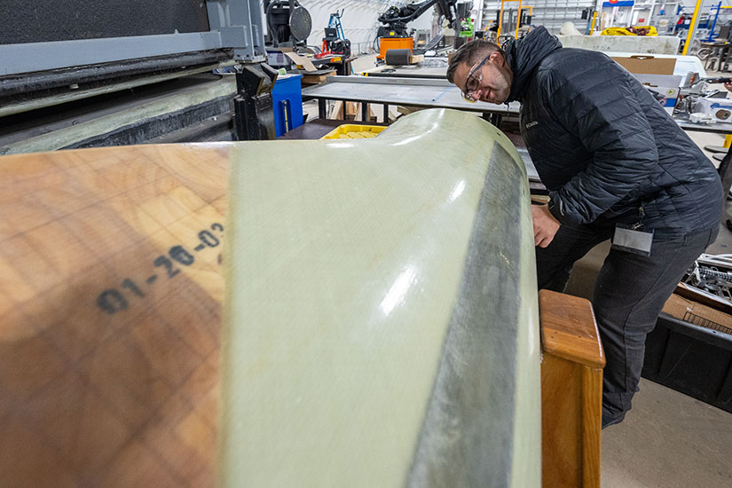 A man in a jacket with safety goggles leans over to examine materials used in building wind turbines.