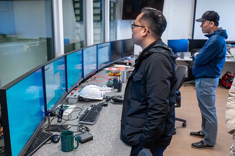 Two men stand in front of a row of computers. 