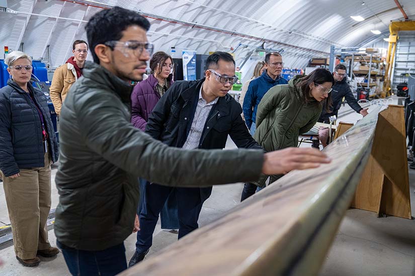 Several people wearing safety goggles lean in to examine and touch a long board.