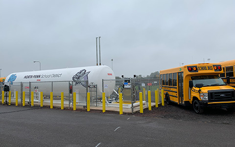 School buses parked next to propane fuel tank.