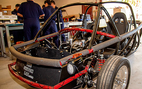 Frame of a go-cart style vehicle with students in the background
