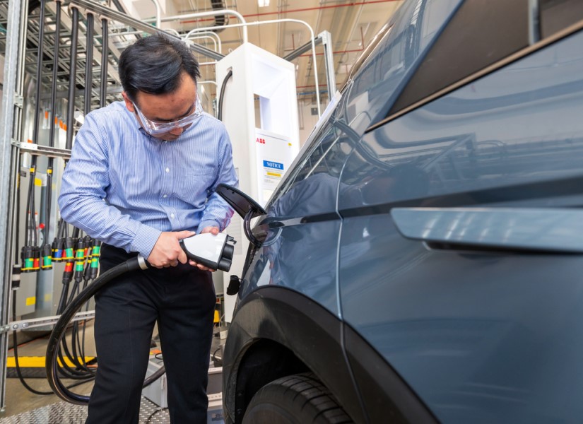 A man plugs a charging cable into an electric vehicle. 