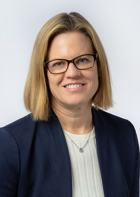 Katherine Hurst smiling, wearing glasses and a blazer.