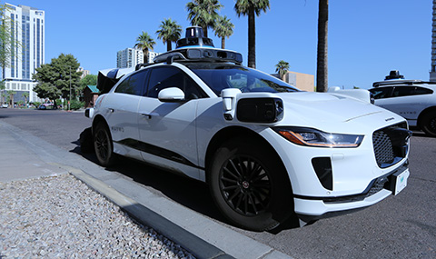 A white Waymo autonomous "robotaxi" pulls up to the curb.