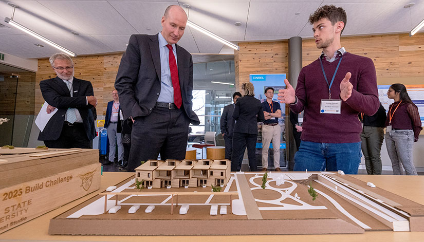 Three men look at a scale model of a zero energy housing complex.
