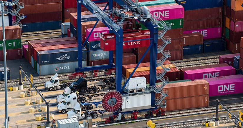 Semi-trucks load colorful shipping containers in a busy port.