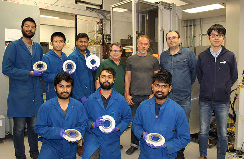 A group of researchers in a lab, most wearing lab coats and gloves and holding disks