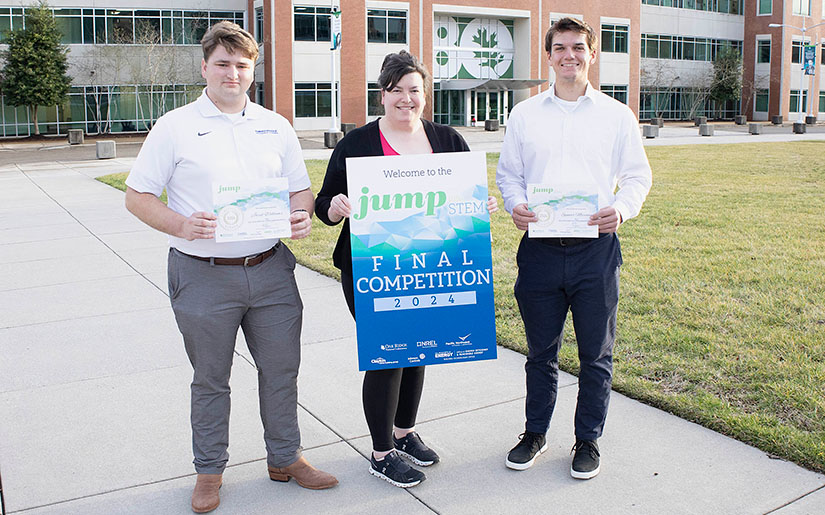 Three people standing outside while holding certificates. 